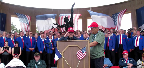 Commemoration ceremony with veterans, flags, and a speaker at the podium
